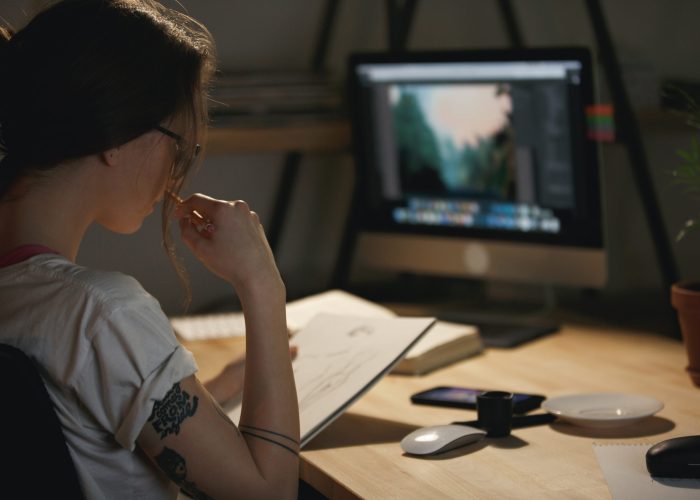 Concentrated young lady designer drawing sketches in album Image of concentrated young lady designer sitting indoors at night drawing sketches in album while using computer.